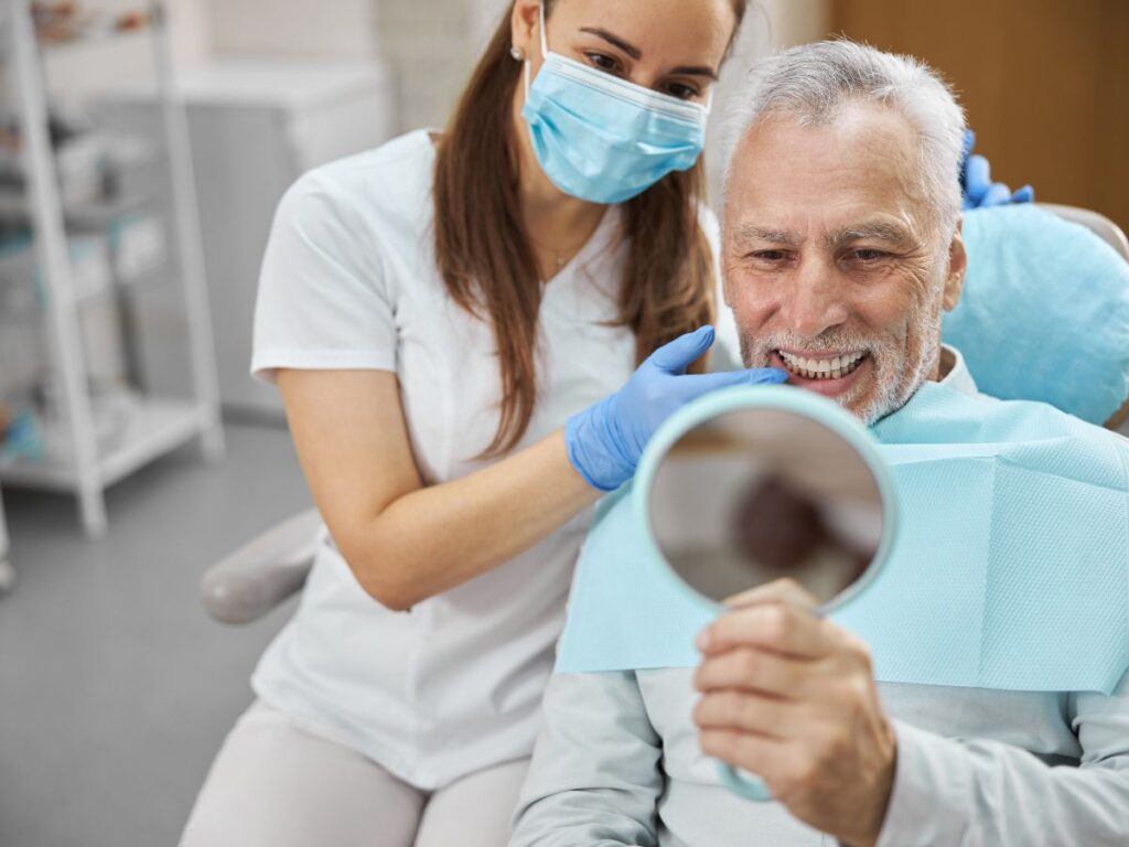 patient of Long Island dental implant specialists viewing his new set of teeth after a all-on-four dental implants procedure